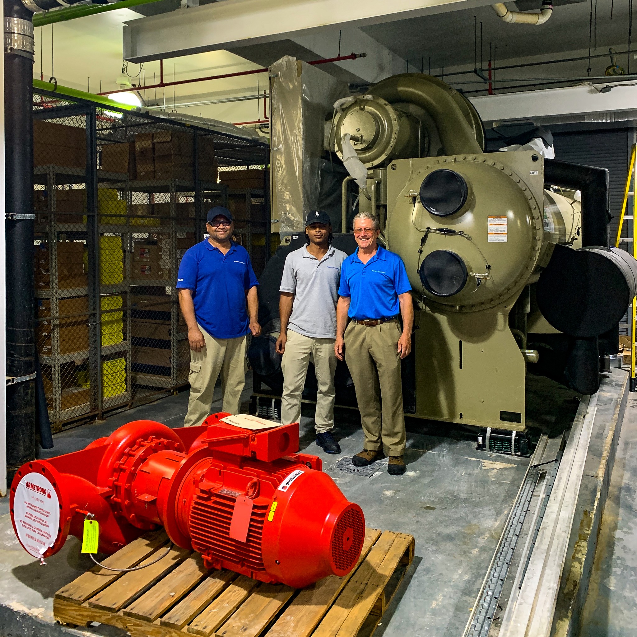 Three men pose in front of water chiller